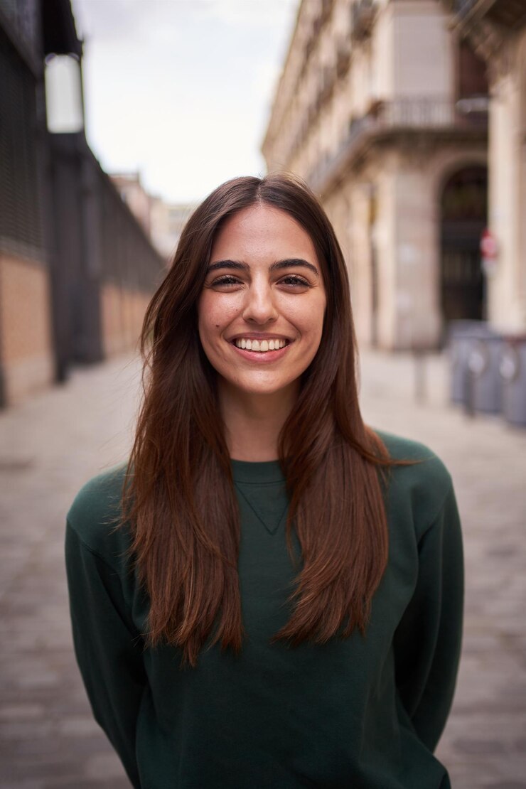 Femme dans la vingtaine brune portant un haut vert dans une rue